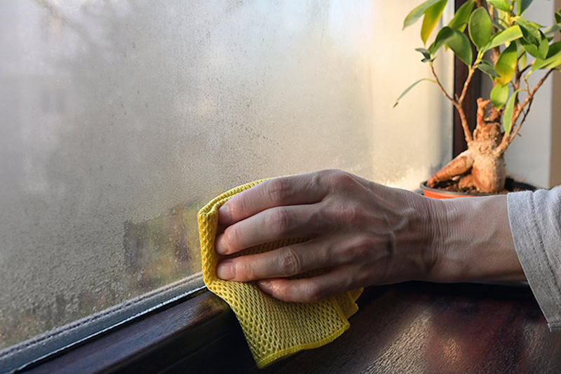 hand wiping condensation off of a kitchen window.